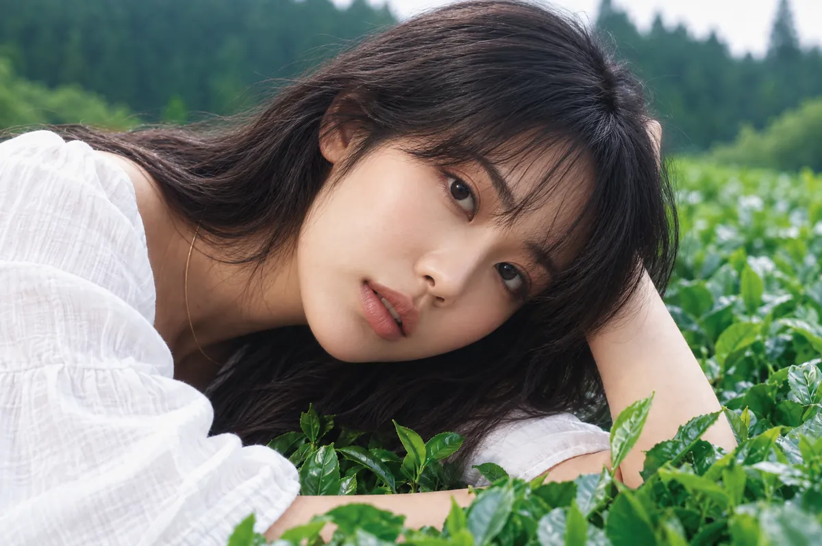 A woman in a white blouse resting her head on her arm in a green tea field